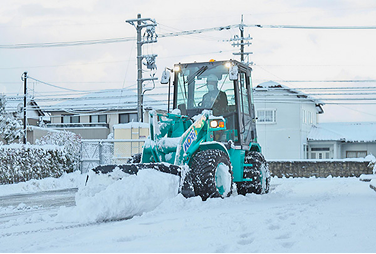 街中の道路で雪を押し除けて除雪作業を行うミニホイールローダ。