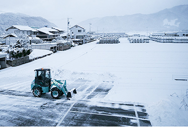 広い敷地内で除雪作業を行うミニホイールローダの遠景。