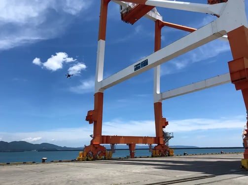 港湾の大型クレーン周辺を点検飛行する小型ドローン。