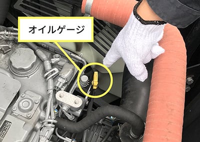 エンジンルーム内の黄色いオイルゲージの取っ手を指差している写真。