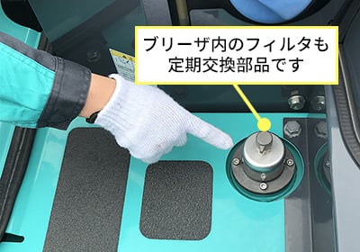 作業員の手がブリーザ内のフィルタ箇所を指差している接写写真。このフィルタも定期交換部品であることを示している。